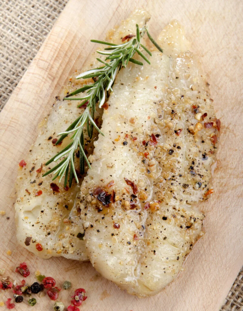 grilled whiting fillet with pepper and rosemary on wooden board