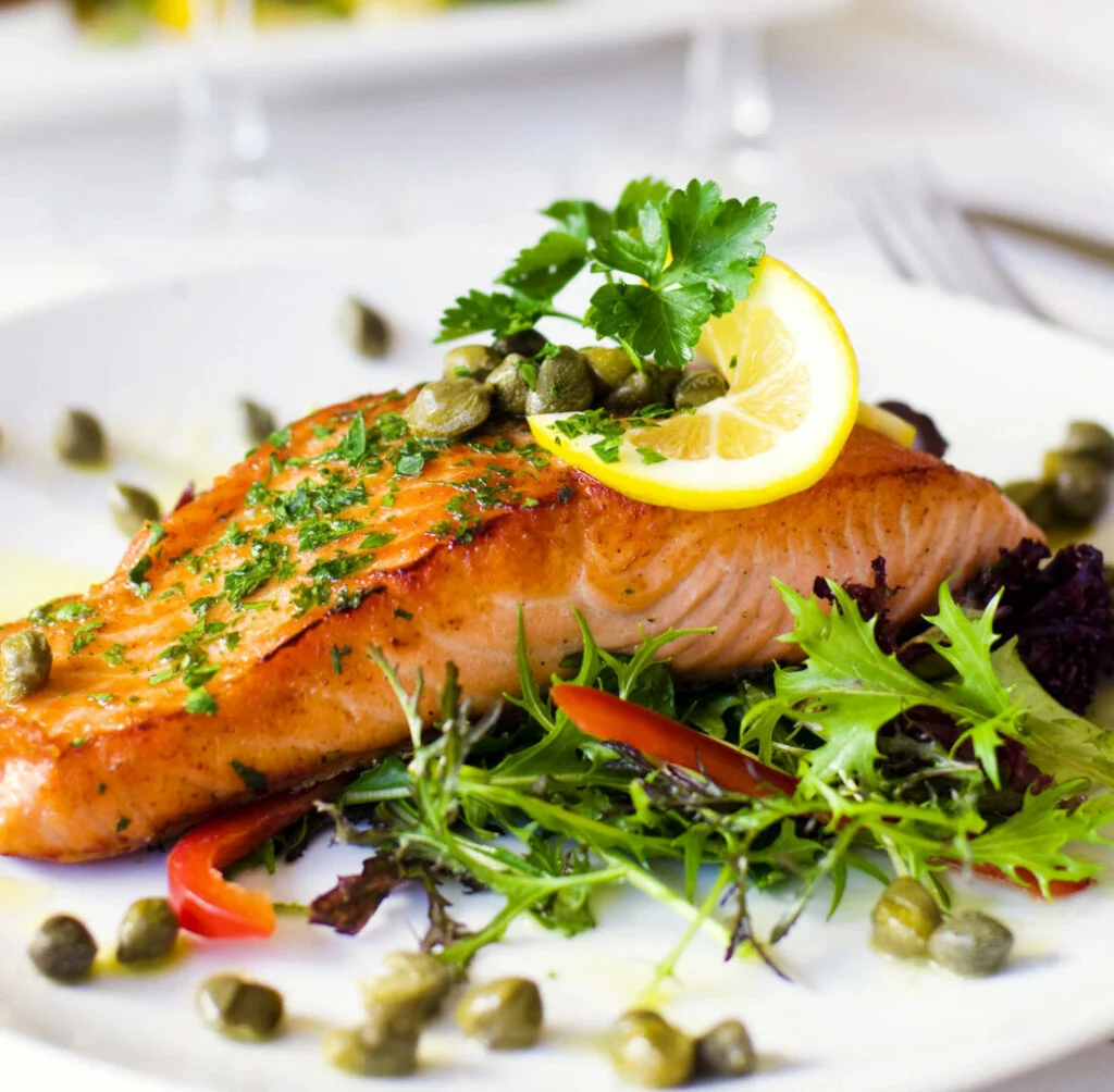 Grilled salmon fillet with vegetables, lemon slices and capers