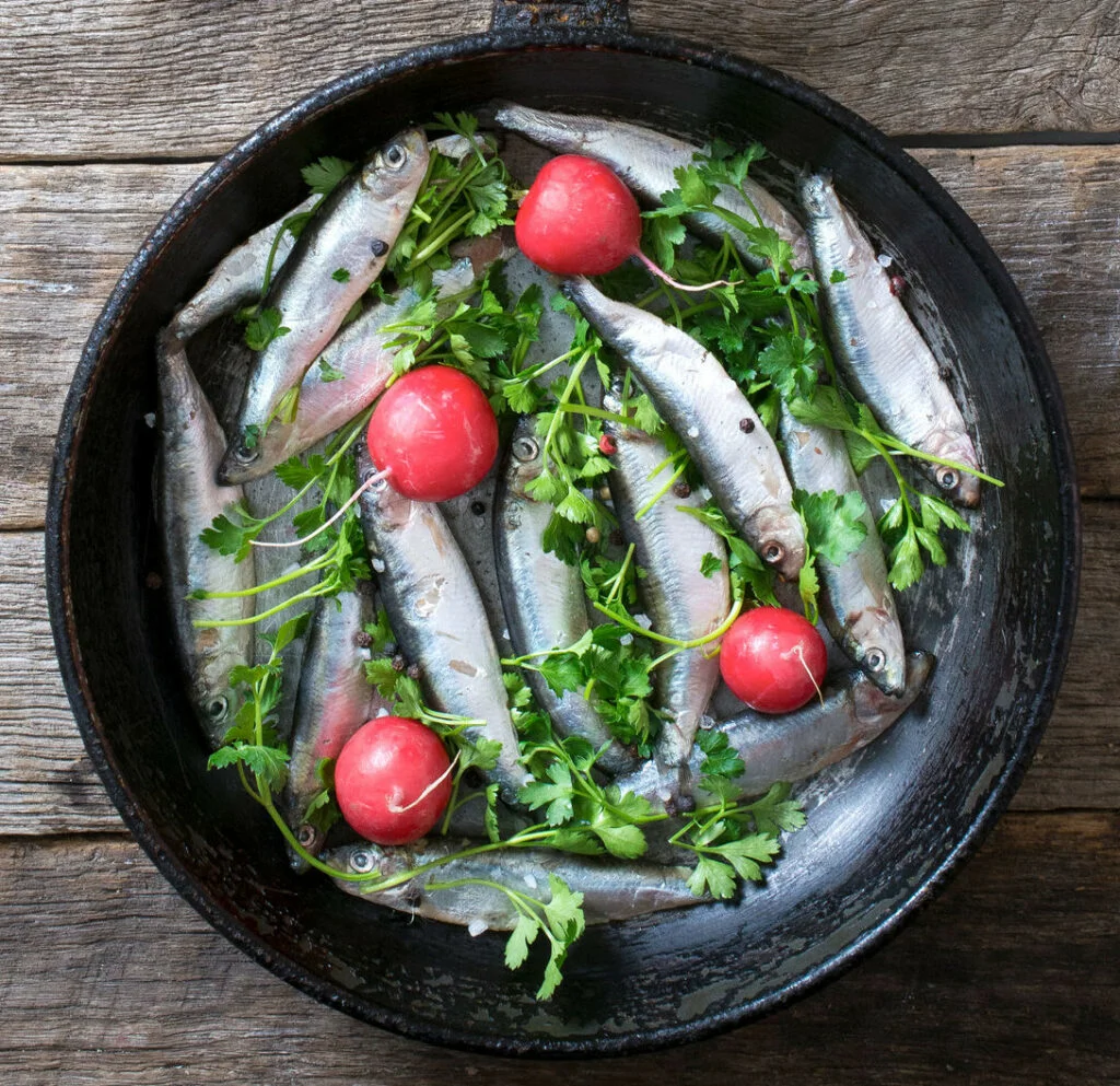 Smelts fish in the pan with radish and parsley on wooden background