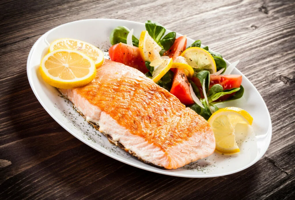 Grilled salmon and vegetables on a plate with lemon slices and veggies