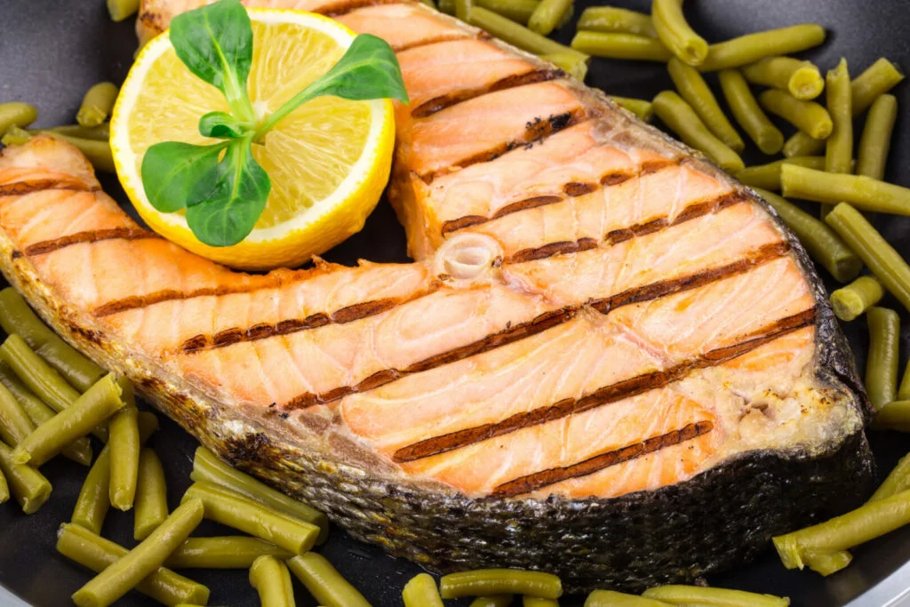 Salmon steak on pan with green beans and a lemon slice.