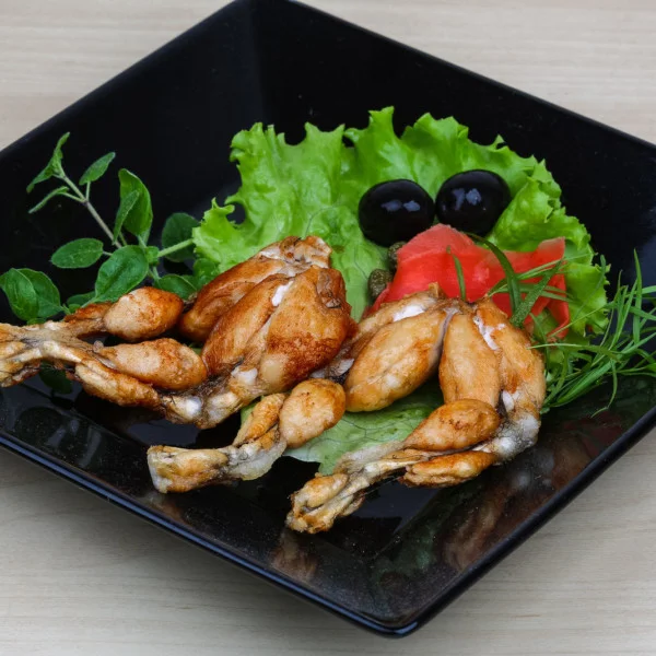Roasted frog legs with herbs and spices, plated with lettuce and fruit.
