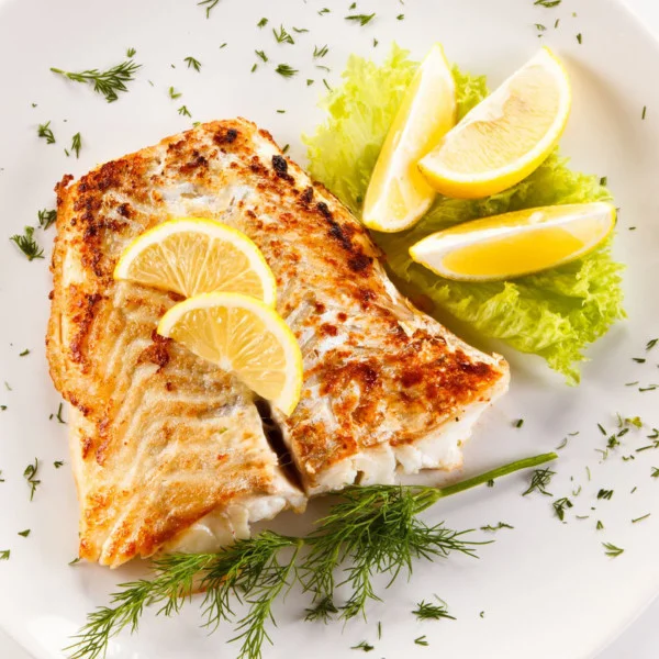 Fried fish fillet and vegetables on a white background with herbs and lemon slices on lettuce.