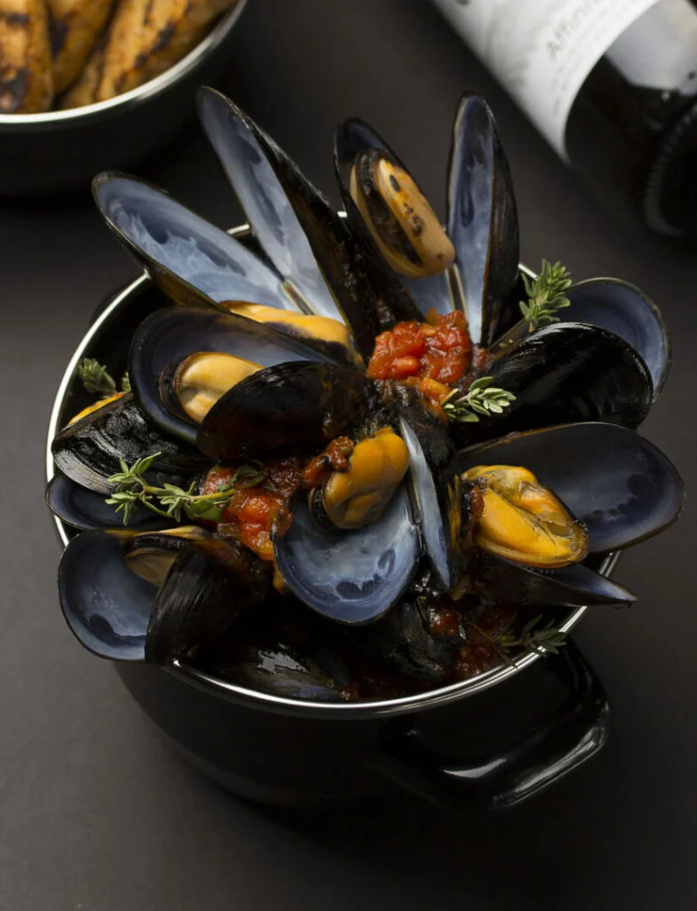 Golden Sun mussels in copper cooking dish and french baguette and wine over black background
