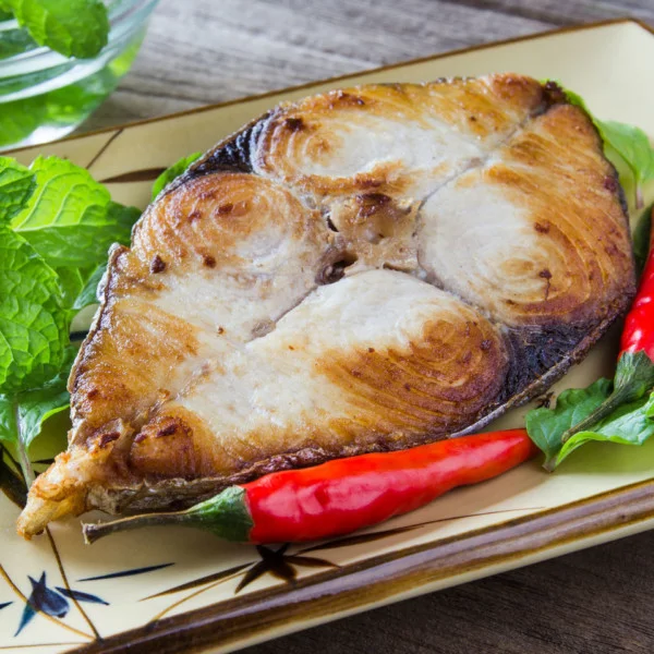 Kingfish steak on a served wooden table with pepper and lettuce.