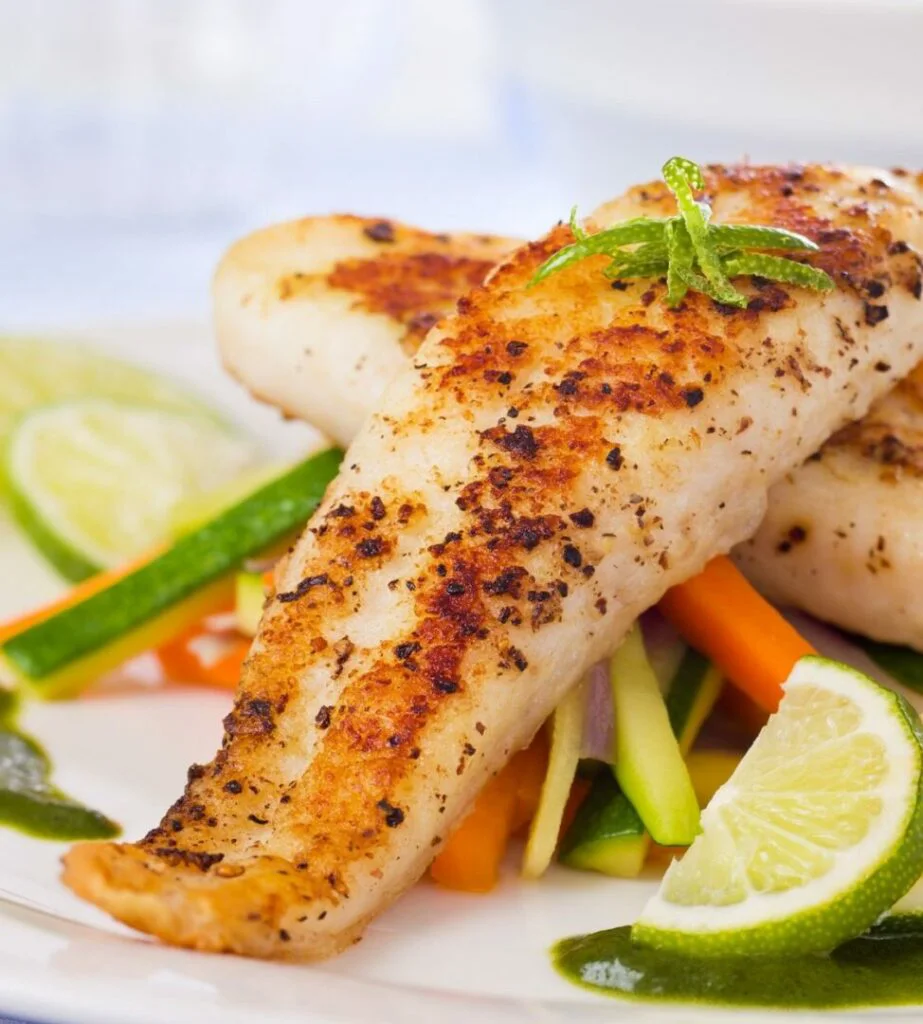 Roasted pangasius fish meal with vegetable on a white plate with lime slices and vegetables